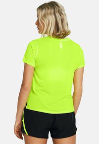 Camiseta corta de manga con un ajuste slim, de un brillante color amarillo neón, con una textura suave y detalles reflectantes en la parte posterior. Llevada con pantalones cortos negros.