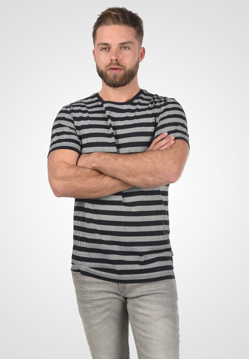 Stripet T-skjorte med horisontale svarte og grå striper, korte ermer og rund hals. Sammen med lysegrå jeans.