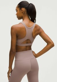 Sport-BH und Leggings-Set in einem gedämpften Mauve-Ton. Konturiert geschnitten mit Racerback-Design und glattem, dehnbarem Material. Minimale Nähte.