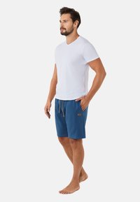 Męski strój składający się z dopasowanej białej bawełnianej koszulki oraz szortów w niebieskim kolorze do kolan z regulowanym trokiem i detalami kieszeni.
