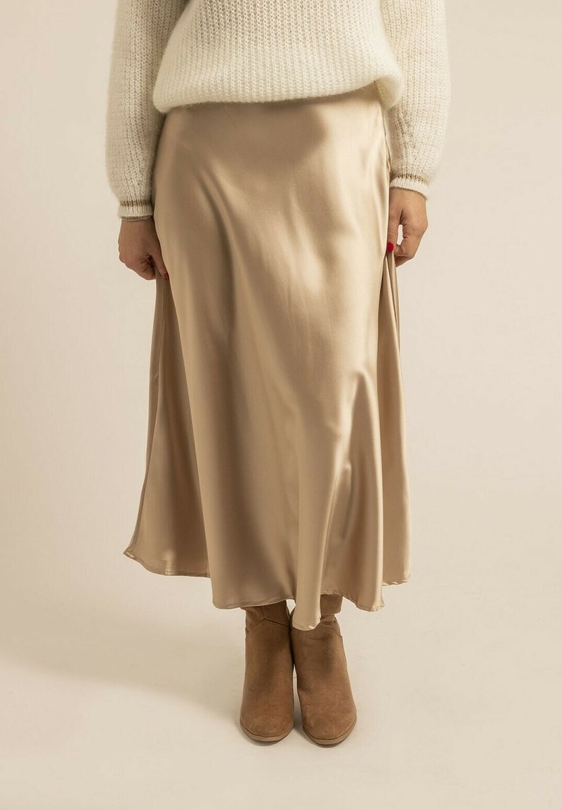 Jupe midi en satin de couleur beige clair, présentant une texture lisse, un design fluide et une fente sur le côté. Associée à des bottines brunes.