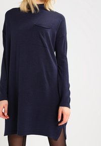 Mörkblå oversize-klänning i mjukt tyg med långa ärmar, rundad halsringning och en liten bröstficka. Kanten har sidospalter.