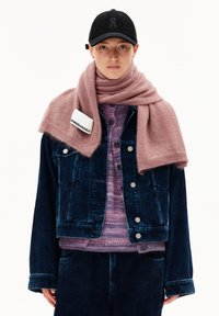 Giacca di jeans in corda blu scuro con bottoni argentati, indossata sopra un maglione a righe viola e completata da una sciarpa a maglia rosa.