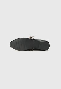 Black flat shoe with a smooth synthetic upper and a sleek, rounded toe. Features a slim ankle strap and a textured rubber sole.