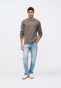 Ruskea, rakenteinen neulepusero, vaaleansiniset farkut ja valkoiset lenkkarit. Neulepuserossa on pyöreä pääntie ja pitkät hihat.