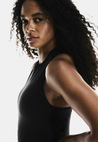 Black athletic tank top featuring a rounded neckline, sleeveless design, and smooth fabric, worn by a person with curly hair.