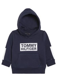 Sudadera con capucha azul marino que presenta un bolsillo canguro frontal, un panel de logo blanco con "TOMMY HILFIGER" y detalles contrastantes blancos en las mangas.
