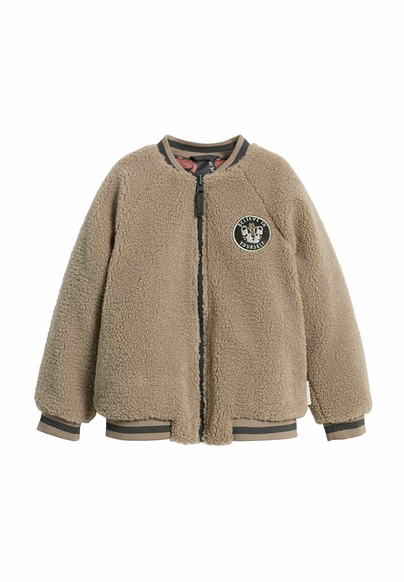 Tan fleecemössa med en rund applikation som har texten "Tro på dig själv", dragkedja, samt randiga ribbade ärmslut och nederkant. Mjuk, texturerad tissu.