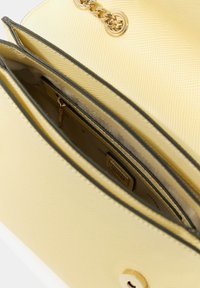 Borsa gialla con texture e dettaglio catena dorata. Presenta due scomparti, uno con tasca con cerniera e un'etichetta rettangolare del marchio all'interno.