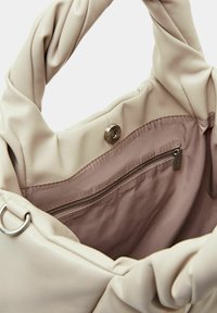 Flødefarvet taske med blødt, knyttet håndtag, med en glat læderudvendig og en satinforet inderside med en lynlåslomme.