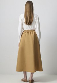 Falda larga beige con cinturilla elástica, hecha de una tela suave. Combinada con una blusa blanca. Calzado plano visible.