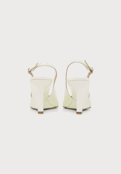 Paire de sandales blanches à talons hauts avec brides à la cheville vues de dos sur un fond clair uni.
