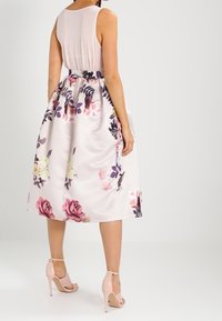 Robe midi florale avec une finition satinée, dotée d'un corsage ajusté, d'une jupe ample, de fleurs rose et violet, et d'une ceinture assortie. Associée à des talons beiges.