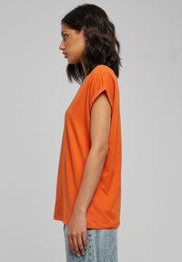 Oranje T-shirt met korte mouwen van zacht katoen, met opgerolde mouwen, een rechte snit en een ontspannen pasvorm. Gecombineerd met lichtblauwe jeans.