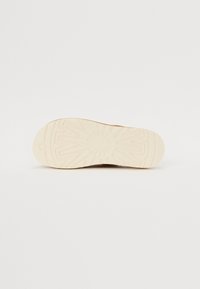 De onderkant van een bruine schoen met een gestructureerde, witte rubberen buitenzool met een zonnestralenpatroon. Gladde randen en een gebogen vorm verbeteren de grip.