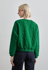 Grüner, gesteppten Sweatshirt mit strukturierten Oberfläche, geripptem Saum und Design mit tiefer gesetzten Schultern, kombiniert mit dunklen Jeans.