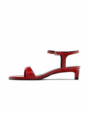 Sandale rouge en cuir à talon bas avec bride de cheville et boucle, bout ouvert et semelle fine sur fond blanc.