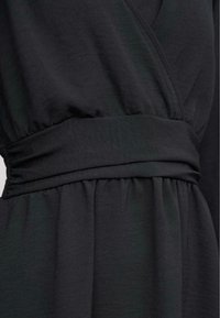 Vestido negro con un diseño envolvente, con cintura fruncida y una tela suave y texturada que crea pliegues y caídas suaves.