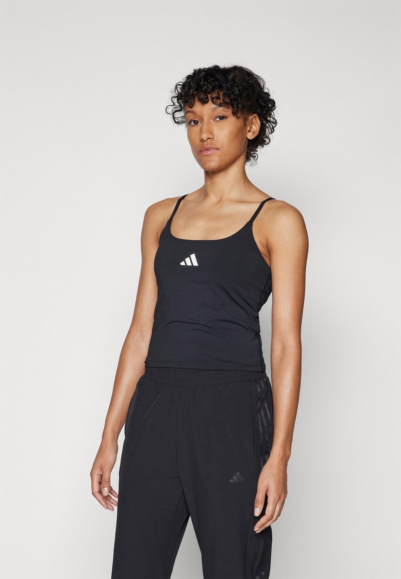 Zwarte sportieve tanktop met dunne bandjes en een ronde halslijn, met een wit adidas-logo op de borst. Gecombineerd met zwarte broeken.