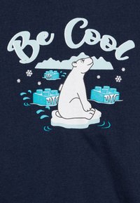 T-shirt blu navy con un orso polare seduto su un iceberg, con il testo "Be Cool" in azzurro chiaro e fiocchi di neve. design grafico, materiale in cotone.