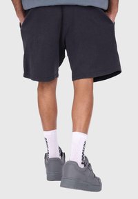 Dunkelgraue Waffelstrick-Shorts mit Taschen, kombiniert mit weißen Socken mit schwarzem Text und grauen Sneakers mit glatter Oberfläche.