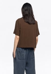 Camiseta corta de manga corta en color marrón con un corte relajado, fabricada en una tela suave, con un dobladillo recto y sin logotipos ni patrones visibles.