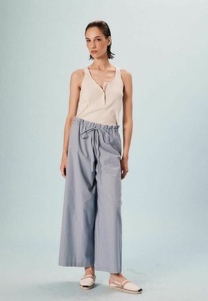 Haut sans manches beige avec un col en V et un petit accent rouge, associé à un pantalon large à rayures bleues et blanches, ample avec une taille à cordon.