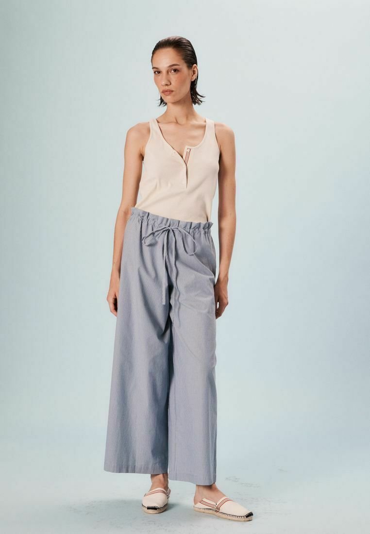 Haut sans manches beige avec un col en V et un petit accent rouge, associé à un pantalon large à rayures bleues et blanches, ample avec une taille à cordon.