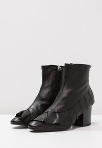 Bottes noires en cuir à la cheville avec fermeture éclair et détails froncés à l'avant. Talon bloc et bout pointu ; texture lisse.