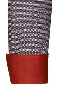 Gemusterter Stoff mit einem geometrischen Design in Dunkelblau, Rot und Creme, an der Unterseite mit einem einfarbigen roten Saum versehen. Weiche Textur.