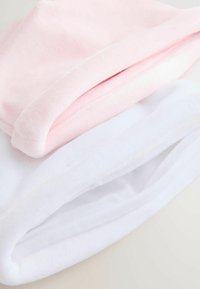 Tessuto in pile morbido e piegato in rosa pallido e bianco, che mette in risalto texture e stratificazione su una superficie chiara.
