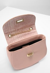 Jasnoróżowa skórzana torebka o zdefiniowanym kształcie. Wnętrze posiada teksturowane wykończenie w wzór krokodyla oraz złoty detal w formie łańcuszka.