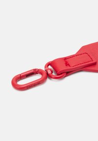 Rotes Lederband mit gebogener Form, ausgestattet mit einem roten Metallkarabinerclip. Der Clip ist mit dem Markennamen "Desigual" graviert.