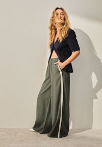 Navy short-sleeve blazer paired with wide, olive green pants featuring a lateral cream stripe. Lightweight fabric with a relaxed fit.