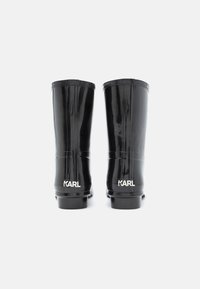 Botas de chuva de borracha pretas com acabamento brilhante, altura até a metade da panturrilha e com parte superior texturizada. Apresenta a marca "KARL" em branco no calcanhar.