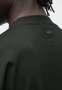 T-shirt de algodão preta com gola redonda. Apresenta tecido texturizado subtil e um logótipo bordado na parte de trás da gola.