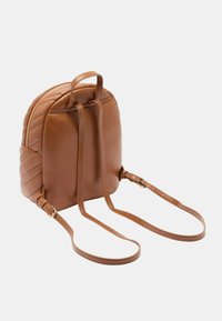 Zaino in pelle marrone con dettagli trapuntati, due spallacci regolabili e chiusura a zip superiore. Forma compatta e arrotondata.