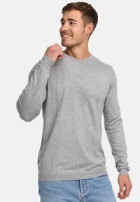 Suéter de manga larga gris claro de cuello redondo con puños y dobladillo acanalados, hecho de tela suave, combinado con jeans de mezclilla azules.