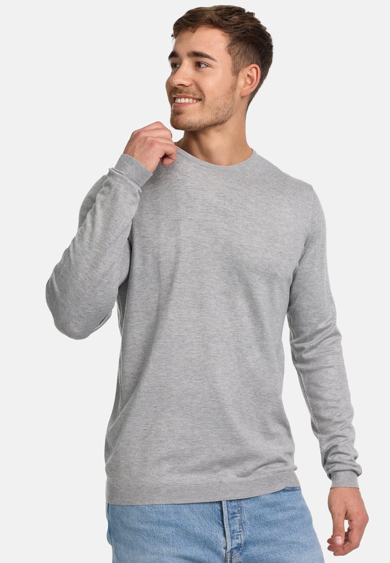 Sweater à col rond à manches longues gris clair avec des poignets et un ourlet côtelés, fabriqué en tissu doux, associé à un jean en denim bleu.