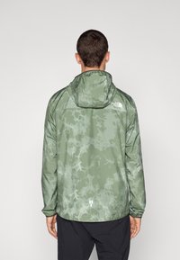 Letvægts grøn tie-dye jakke med hætte. Har elastiske manchetter og et logo på den øverste ryg. Materialet ser glat og vandafvisende ud.