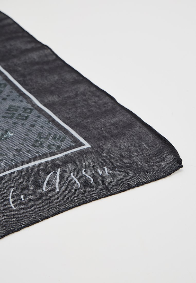 Czarny szalik o teksturowanym wykończeniu, z geometrycznym wzorem w odcieniach szarości oraz białym brzegiem, zawierający szczegóły tekstowe w druku.