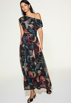 Donna che indossa un abito nero monospalla con stampe colorate celesti e animali, abbinato a sandali neri con tacco e punta aperta.
