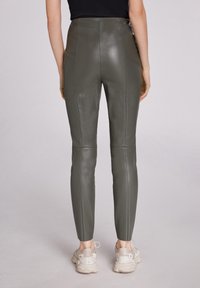 Hooggewaadde leggings in olijfgroen leer met een gladde textuur en naaddetails, gecombineerd met lichtgekleurde sportschoenen.
