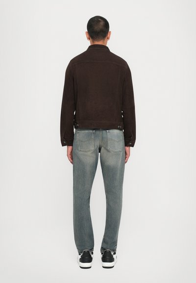 Veste en daim marron à coupe droite, assortie avec un jean bleu délavé et des baskets noir et blanc, vue de dos.