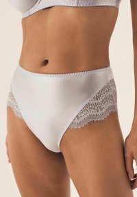Białe majtki z wysokim stanem wykonane z satyny, z koronkowym wykończeniem po bokach, posiadające delikatne falbanki i misterną koronkową dekorację.