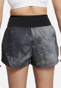 Crne sportske kratke hlače s tie-dye uzorkom u nijansama sive boje. Lagani materijal, elastična kačica u struku i bočni džepovi vidljivi.