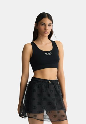 Crop top nero con logo, abbinato a una gonna nera trasparente con un motivo ripetuto e una cintura elastica. Tessuto liscio.