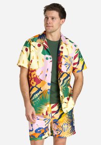 Short-sleeve shirt and shorts set made of vibrant, multi-colored fabric featuring abstract shapes, tropical leaves, and a relaxed fit.