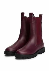 Pareja de botines Chelsea de cuero rojo oscuro con suelas gruesas negras y paneles laterales elásticos, con tiradores en la parte superior.