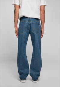 Niebieskie dżinsy z denimu o luźnym kroju, z dwoma tylnymi kieszeniami i subtelnymi przeszyciami, zestawione z białymi trampkami.